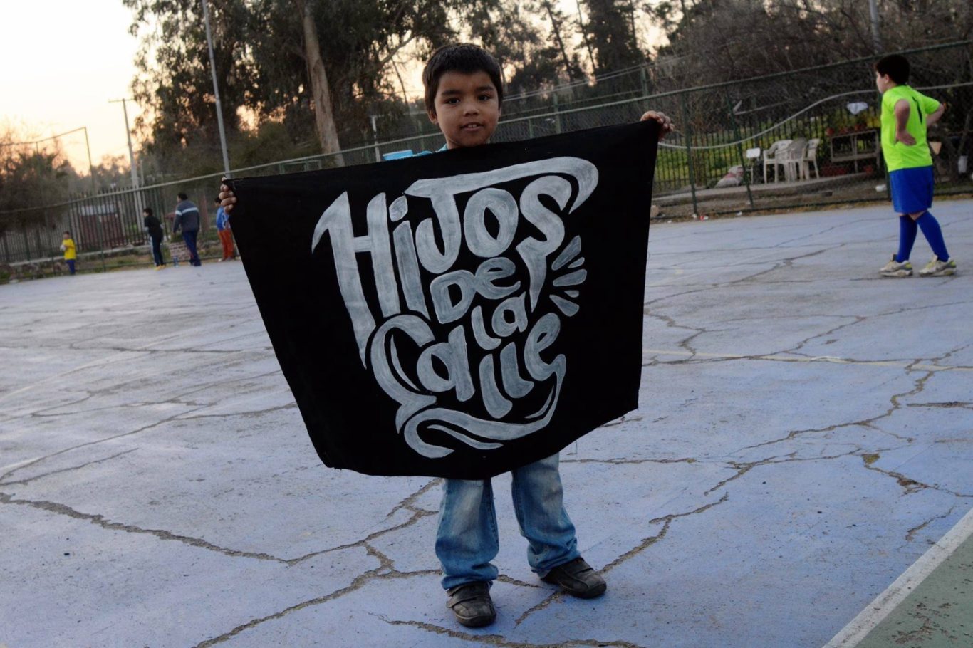 Ein Junge hält ein großes schwarzes Banner mit dem Text "Hijos de la Calle".