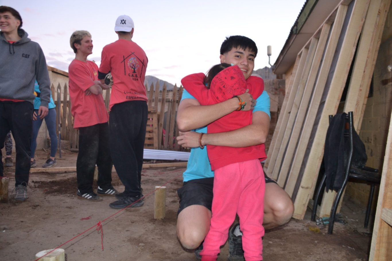 Ein junger Mann umarmt ein kleines Kind in einem Bauumfeld.