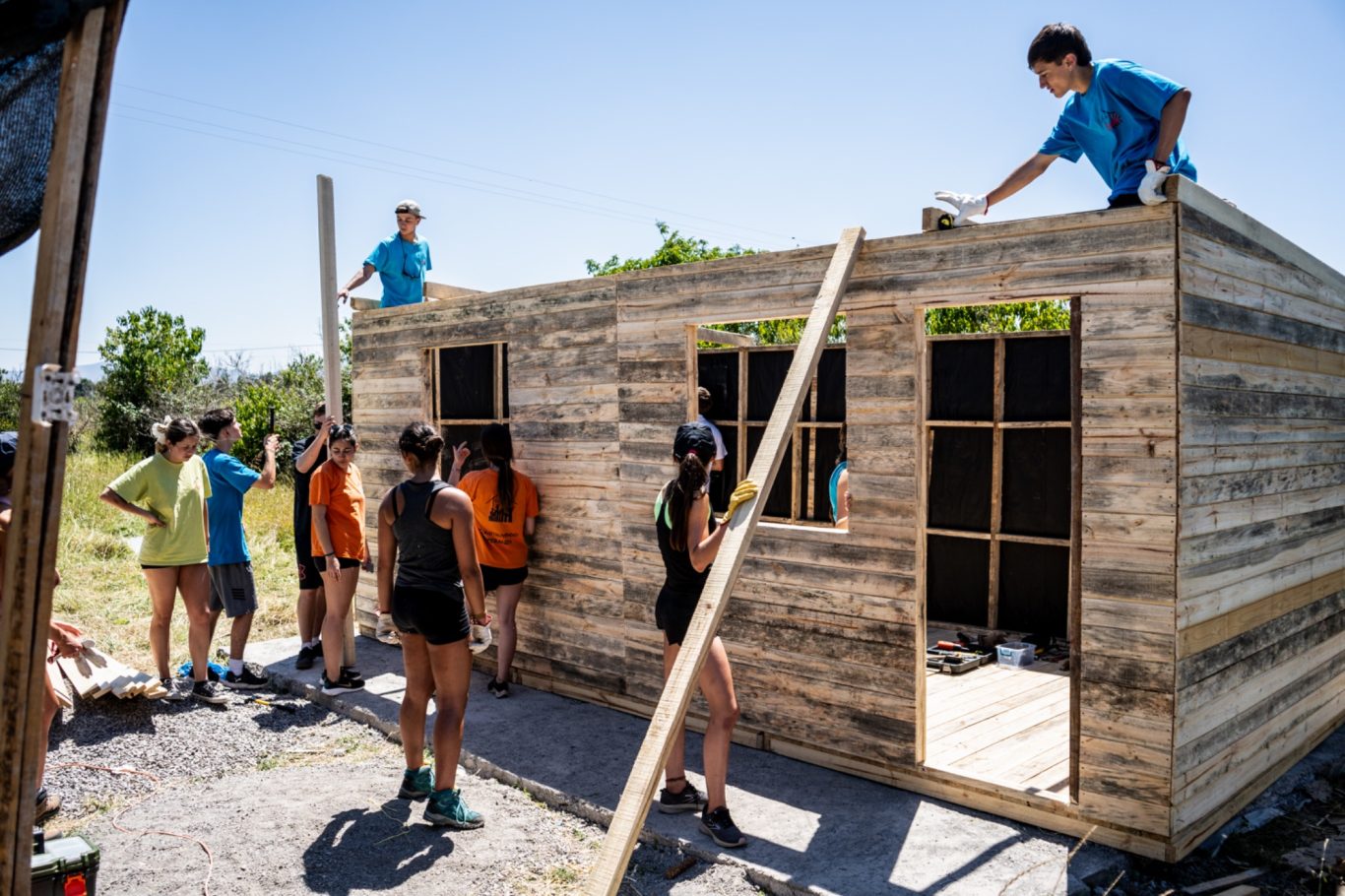 Gruppierung von Menschen, die gemeinsam an einem Holzhaus arbeiten.