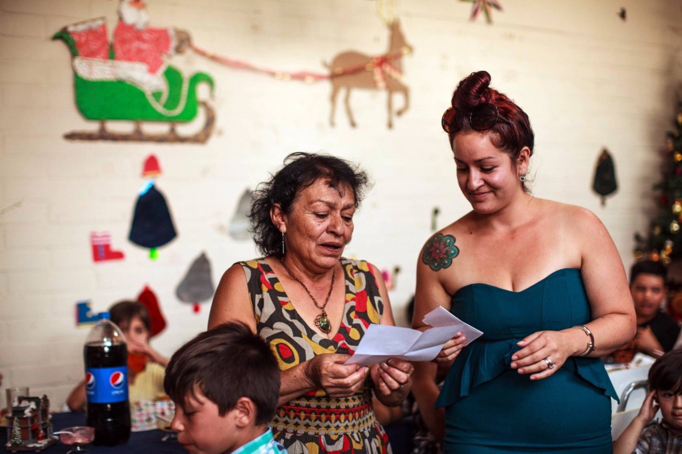 Zwei Frauen lesen einen Zettel, während im Hintergrund weihnachtliche Dekoration zu sehen ist.