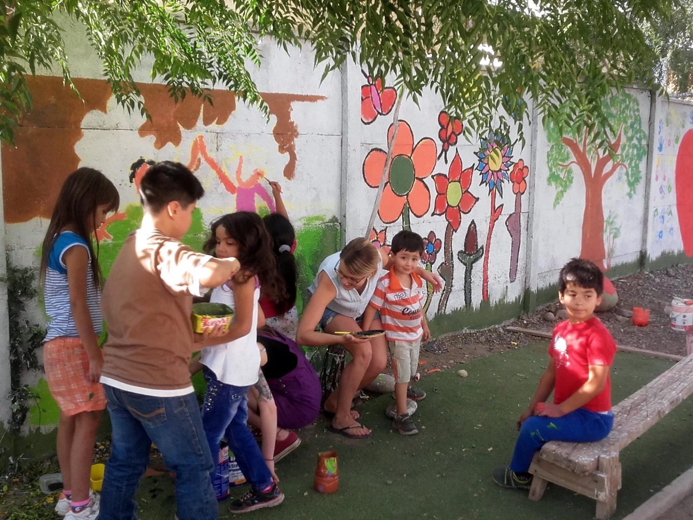 Kinder spielen und malen an einer Wand mit bunten Blumen und Bäumen im Freien.