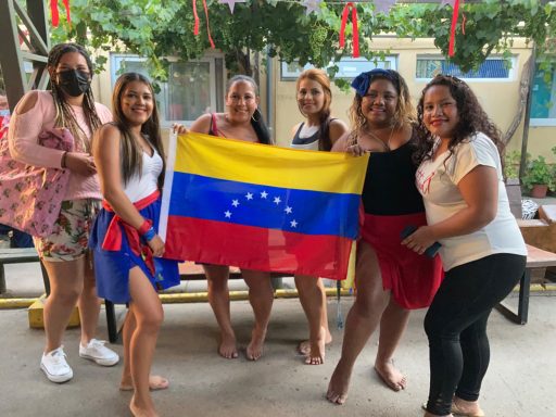 Sechs Frauen halten eine venezolanische Flagge und posieren vor festlicher Dekoration.