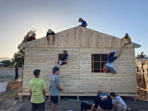 Eine Gruppe von Menschen baut gemeinsam ein Holzhaus im Freien.