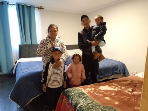 Familie mit fünf Personen in einem Schlafzimmer, lächelnd vor zwei Betten.