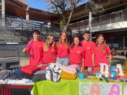 Sechs Personen in roten T-Shirts stehen vor einem Tisch mit bunten Waren im Freien.